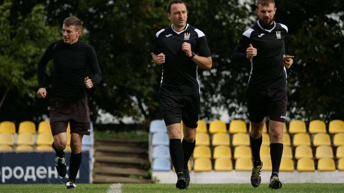 Three male referees running during a training session on a soccer field outdoors.